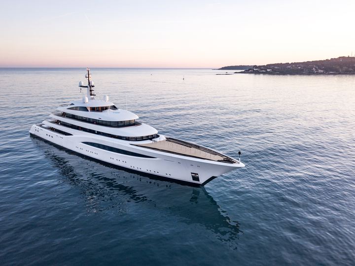 The white Feadship motor yacht Faith cruising on calm water at sunset