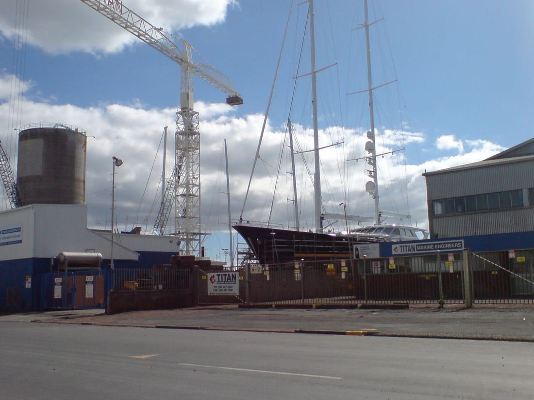 A large sailing superyacht out of the water in a shipyard for maintenance, with cranes nearby