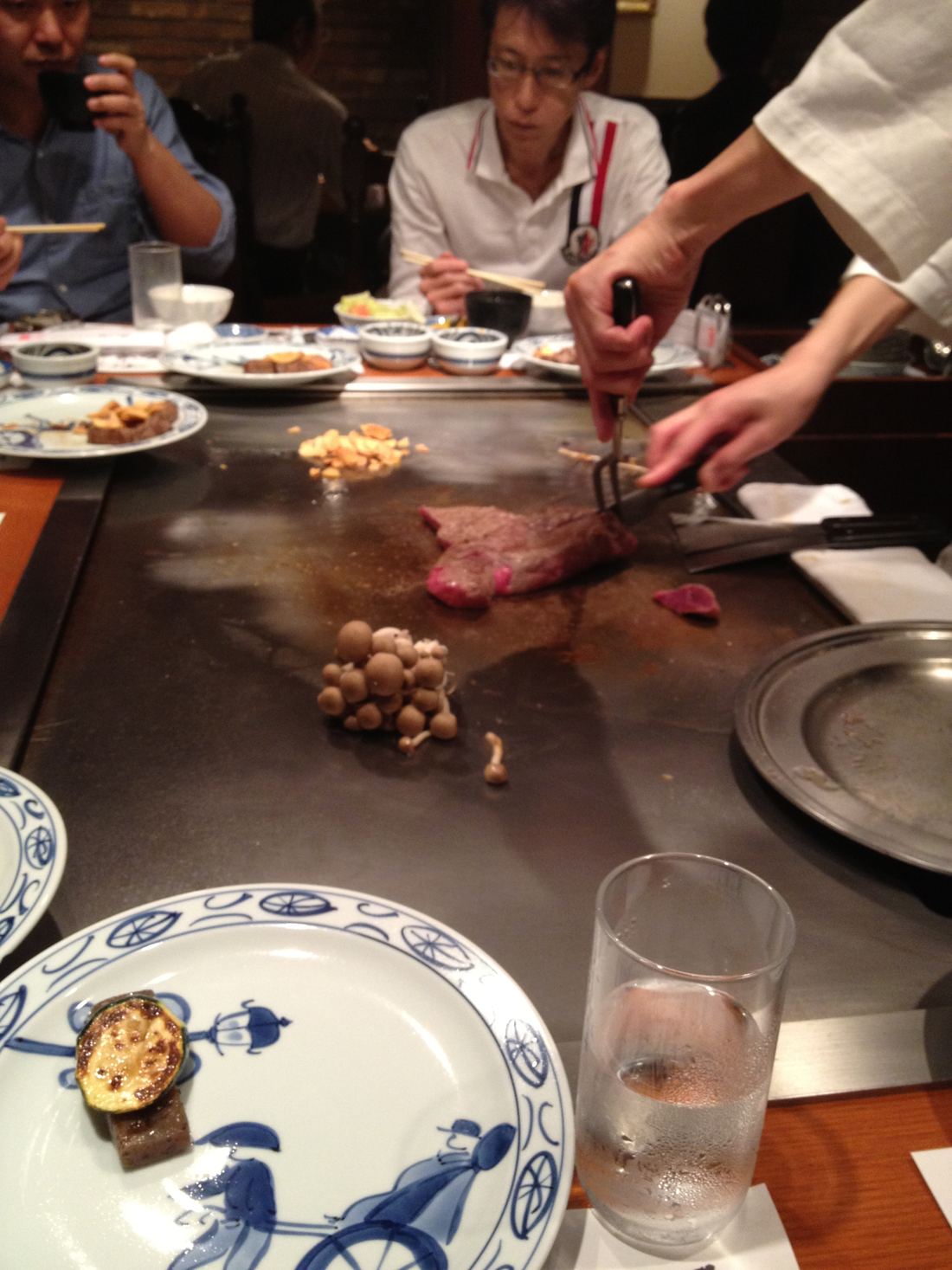 A chef slicing Kobe beef on a teppanyaki griddle in front of diners