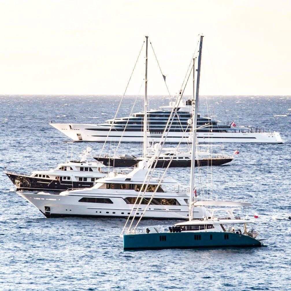 Several superyachts and a sailing yacht anchored in the blue water off Monaco