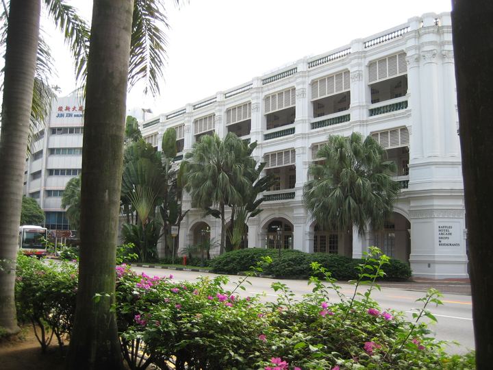 The white facade of Raffles Hotel Singapore framed by palm trees and tropical gardens