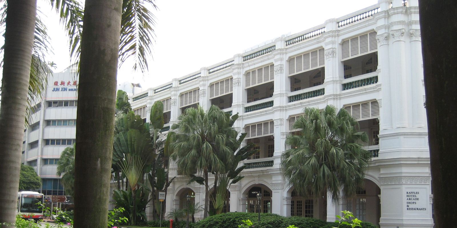 The white facade of Raffles Hotel Singapore framed by palm trees and tropical gardens