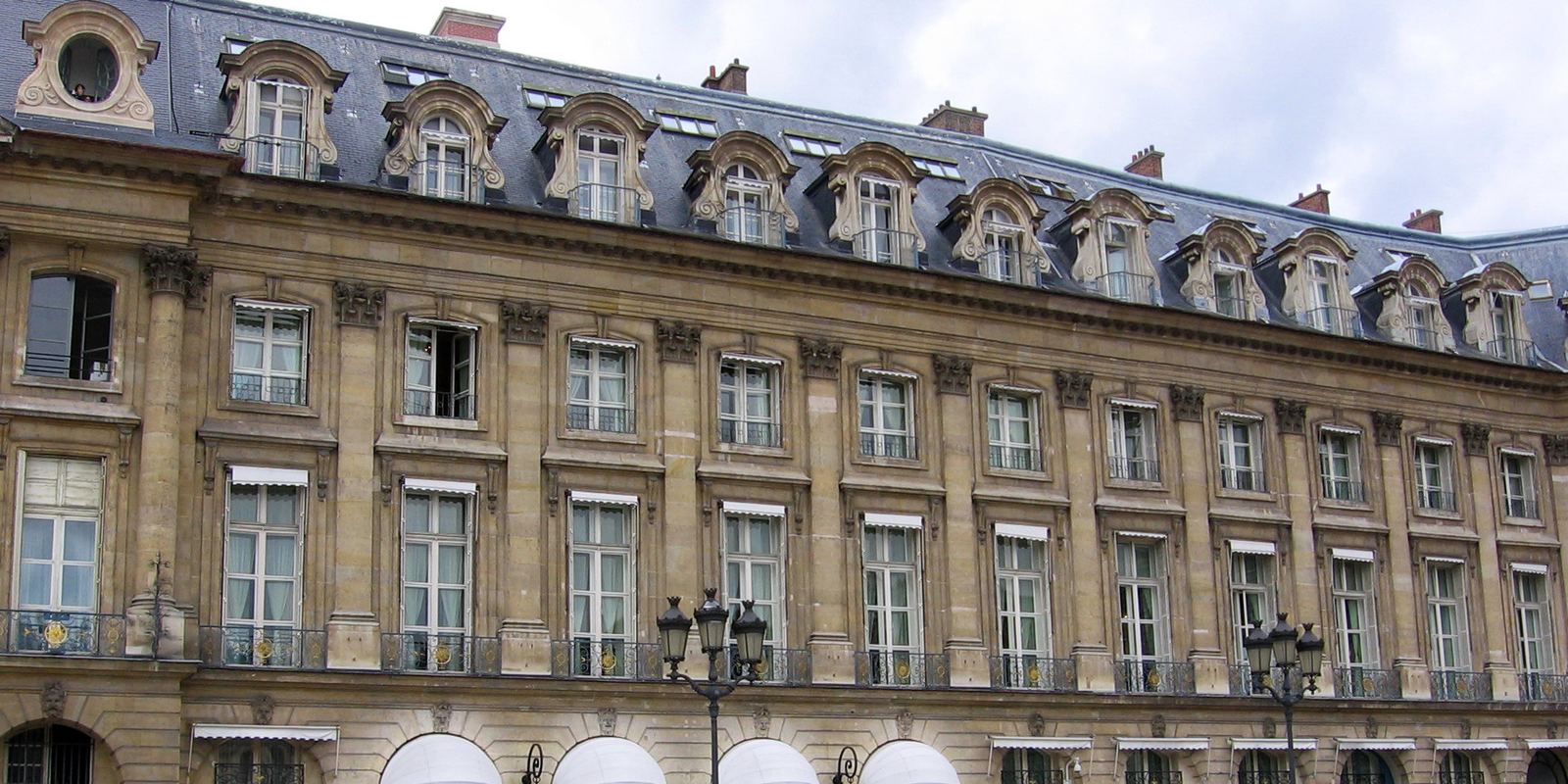 The stone facade of the Hôtel Ritz Paris with white awnings over its arched entrances
